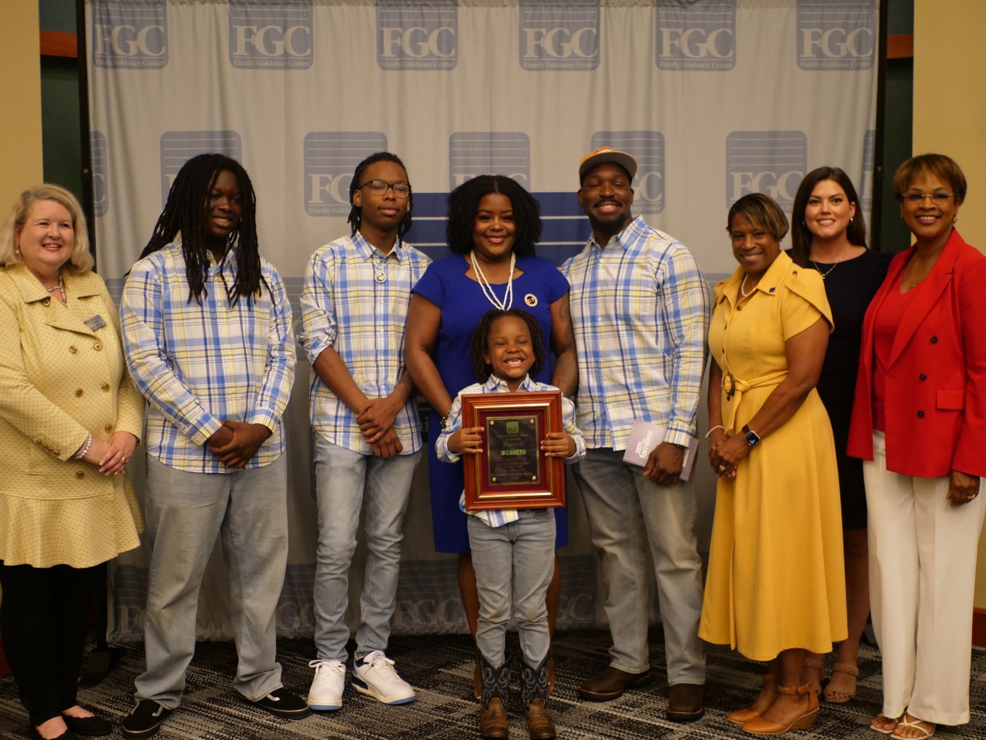 A group of people are posing for a picture with a little girl holding a plaque.