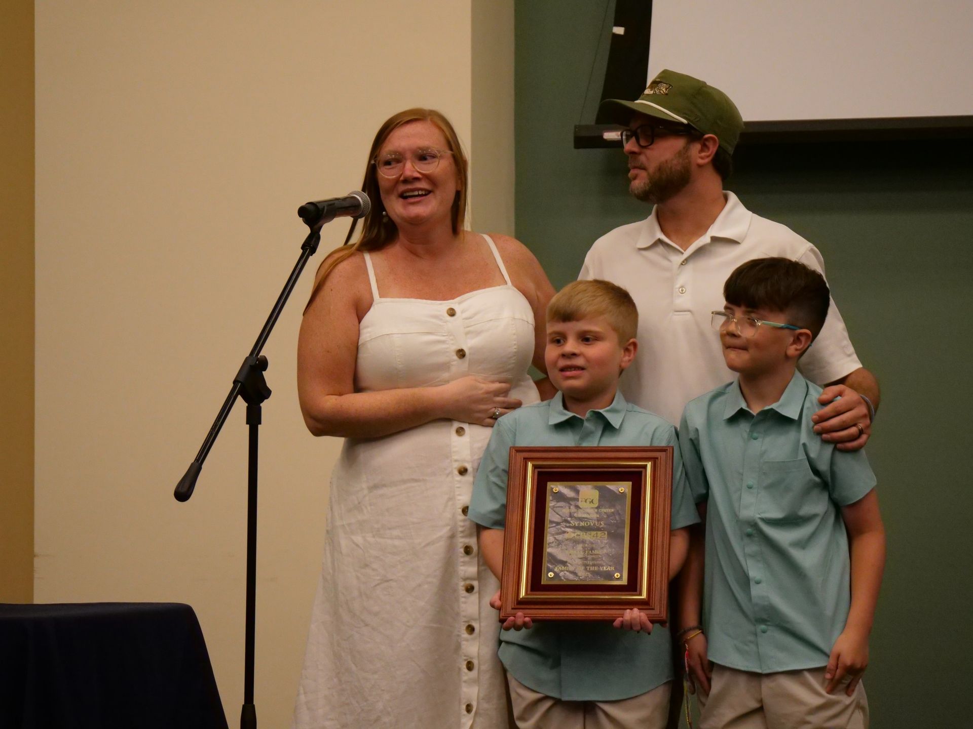 A family is standing in front of a microphone holding a framed picture.