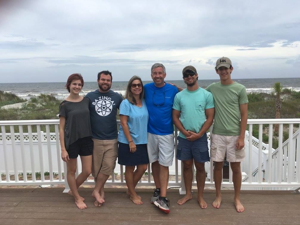 A group of people are posing for a picture on a balcony overlooking the ocean.