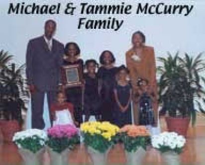 A family is posing for a picture in front of flowers.