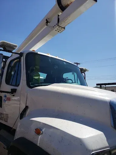 White utility truck with an extended arm, under a blue sky.