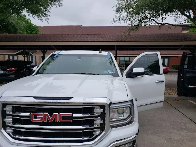 White GMC truck with open door parked under a covered area, red GMC logo.