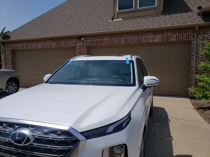 White car parked in front of a house with a brown garage door. Blue tape on the car's windshield.