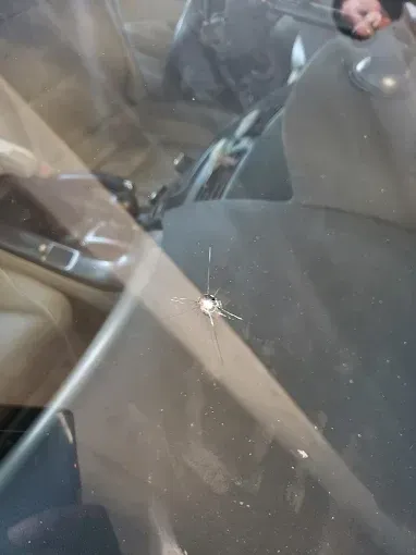 Windshield with a star-shaped crack. Interior of a car visible. Person in the background.
