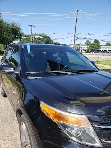 Black SUV parked outdoors with blue tape on the windshield. Sunny day.