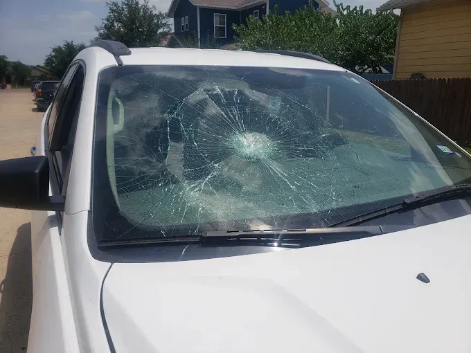 White car with shattered windshield parked on a street.