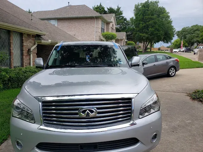 Silver Infiniti SUV parked on a residential street. Another car and houses are in the background.