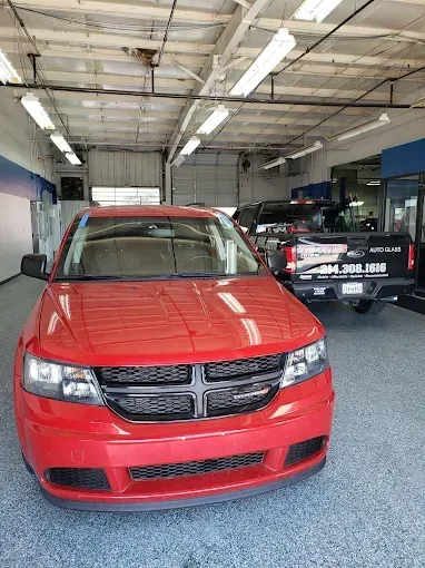 Red Dodge Journey SUV inside a car service bay. Black pickup truck and blue trim visible in the background.