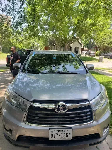 Silver Toyota Highlander parked on a driveway with a person standing beside it. Trees in background.