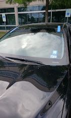 Black car windshield with blue and white stickers. Building and trees in the background.