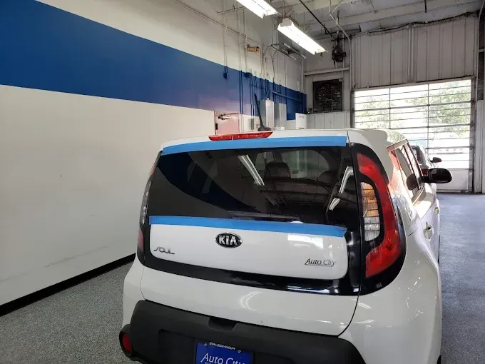White Kia Soul car in a garage, taped for work; blue and white wall backdrop.