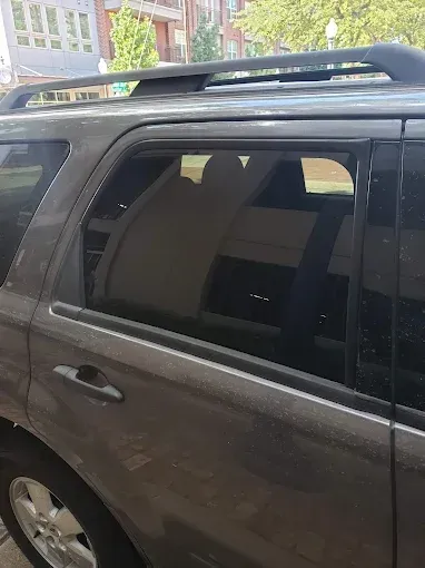 Gray SUV, back window partially open. Sunlight reflects interior seats. Building in background.