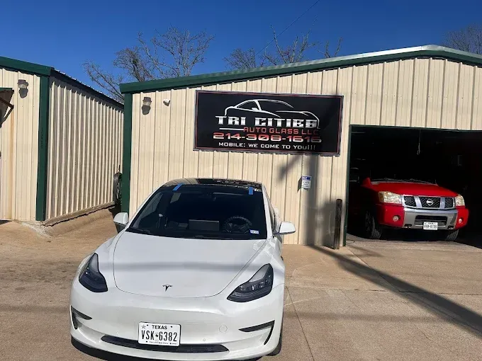 White Tesla parked in front of auto repair shop with a red truck inside the garage.