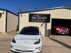 White Tesla parked in front of auto repair shop with a red truck inside the garage.