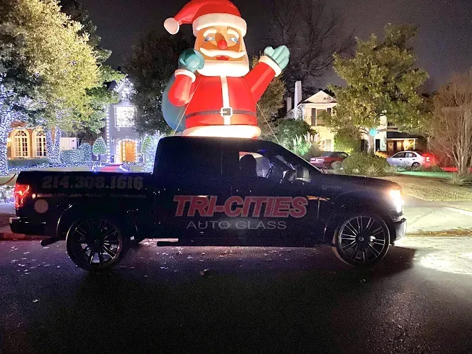 A black truck with a large inflatable Santa Claus on top, parked on a residential street at night.
