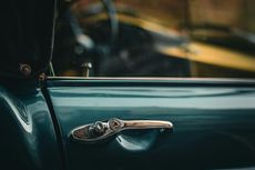 Close-up of a vintage teal car door with a chrome door handle.