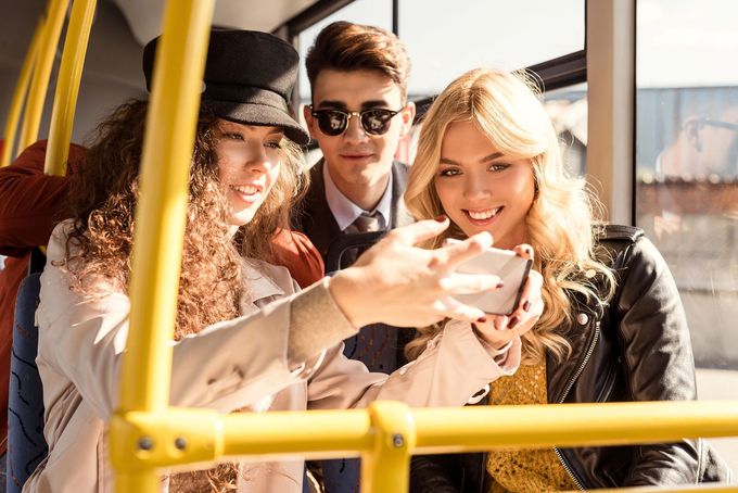 Tre amici su un autobus si scattano un selfie, sorridendo sotto la luce del sole.