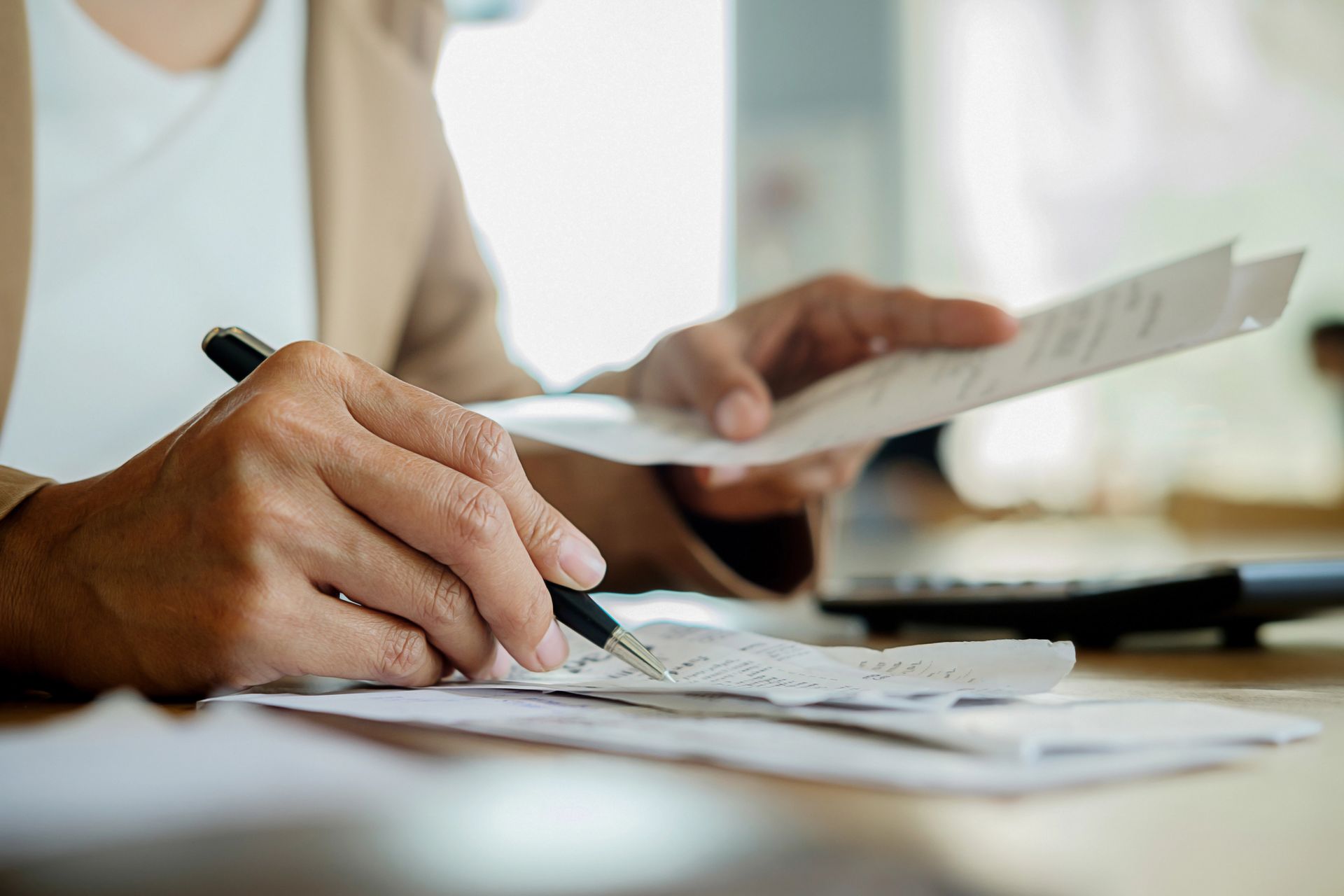 Mani che scrivono su dei fogli a una scrivania mentre un'altra persona esamina un documento.