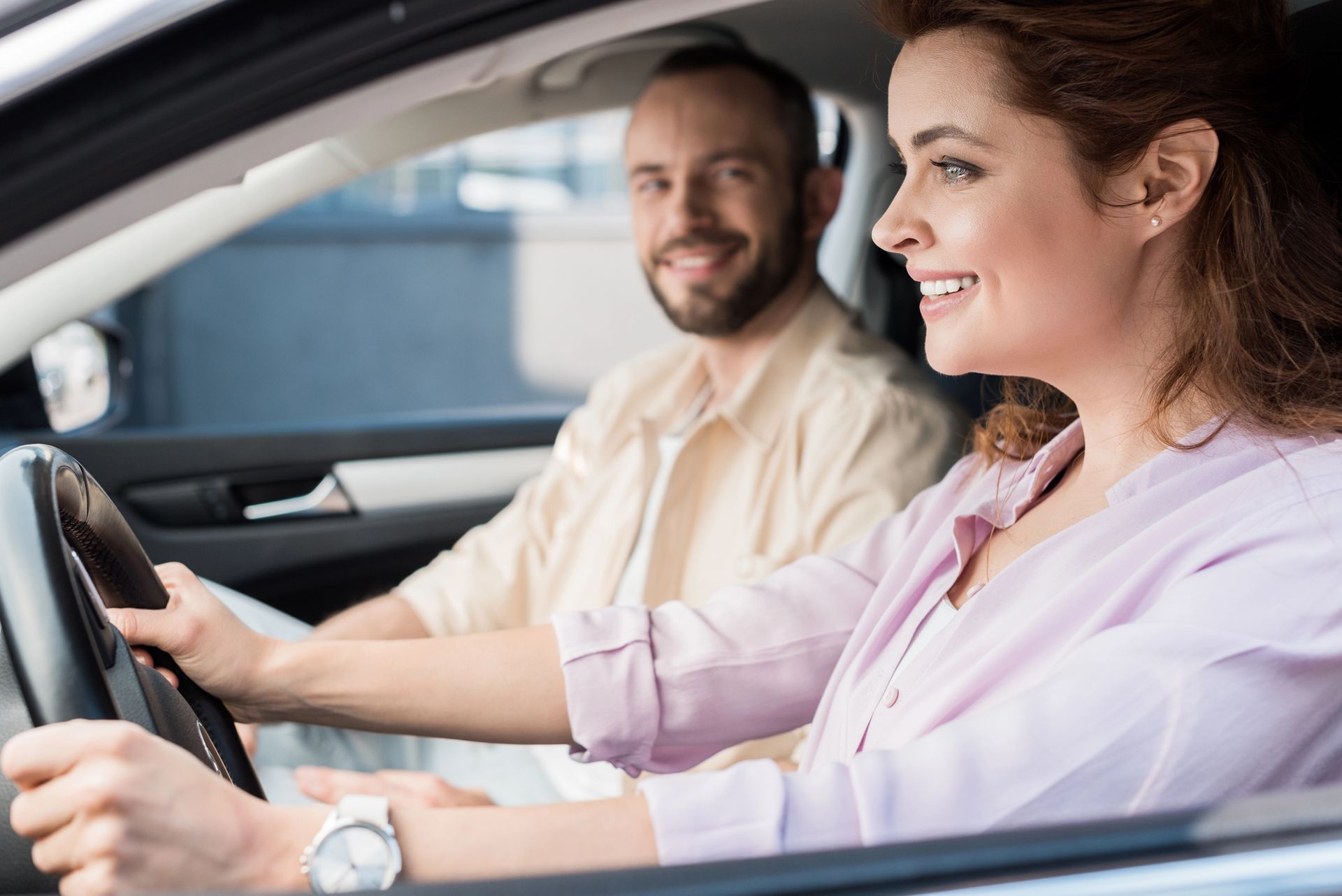 Due persone sorridenti in macchina, con la donna alla guida e l'uomo seduto sul sedile del passeggero.