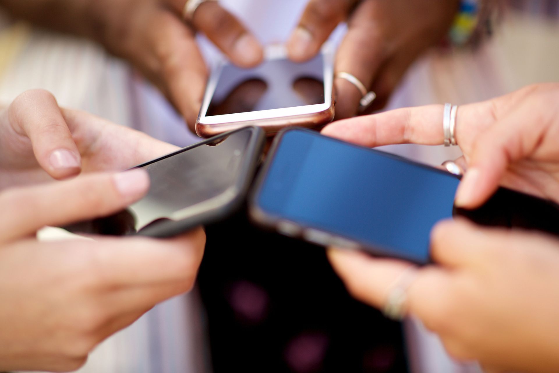 In una scena ravvicinata, si vedono delle mani che reggono degli smartphone attorno a un piccolo oggetto quadrato bianco.