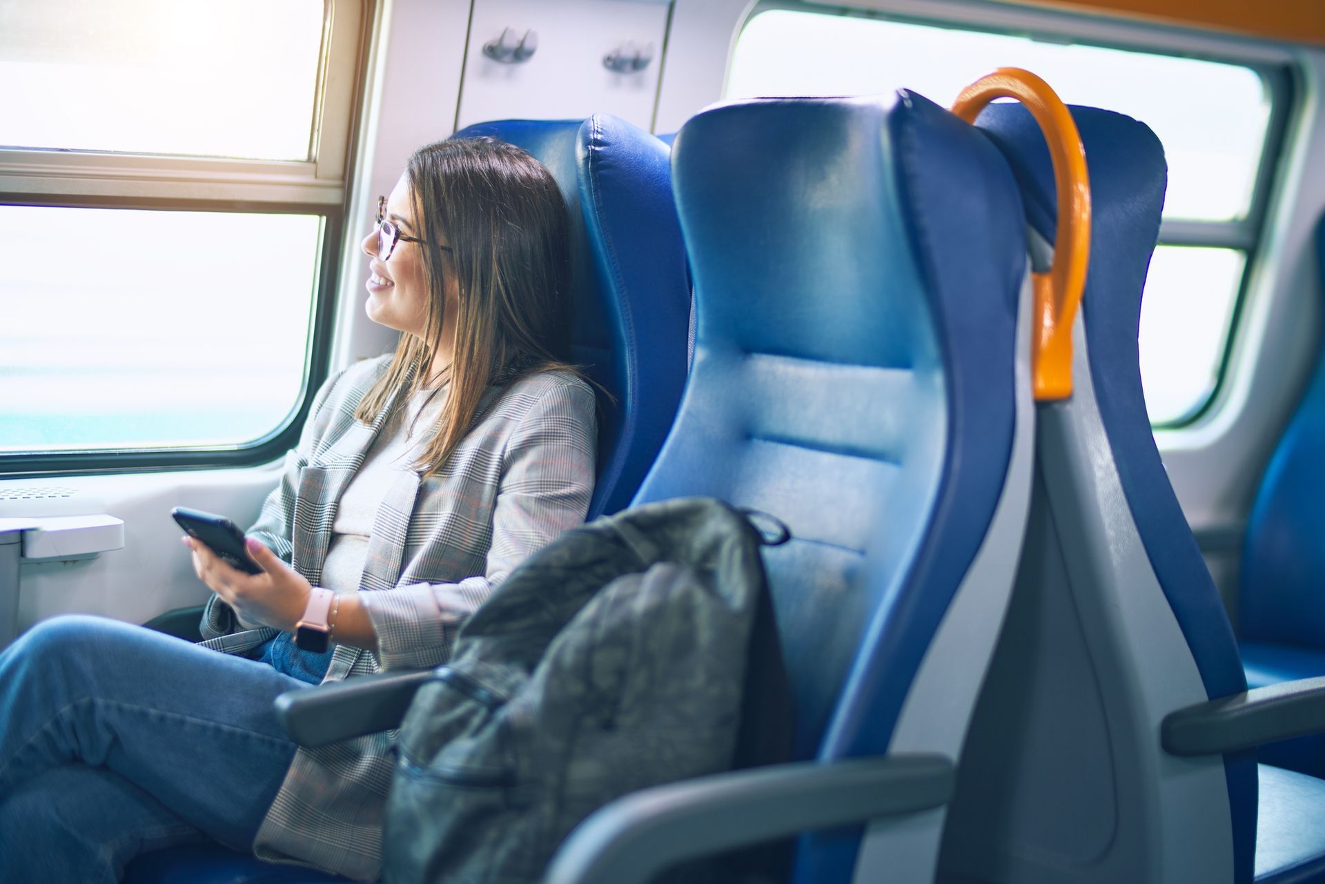 Un passeggero seduto su un sedile del treno guarda fuori dal finestrino e usa il suo smartphone.