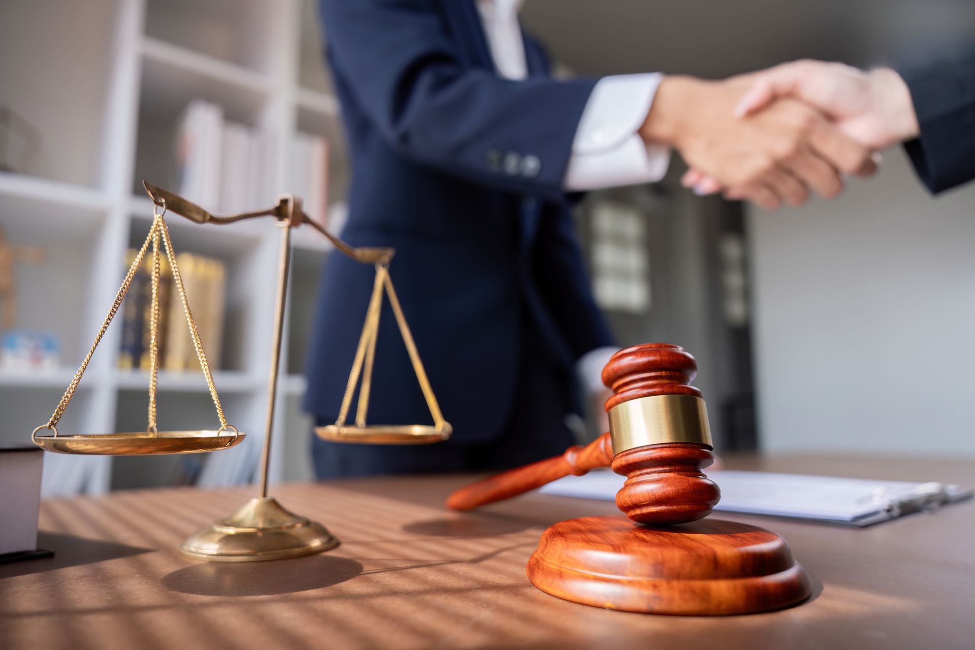 A judge shaking hands with a client in front of a scale of justice and a gavel.