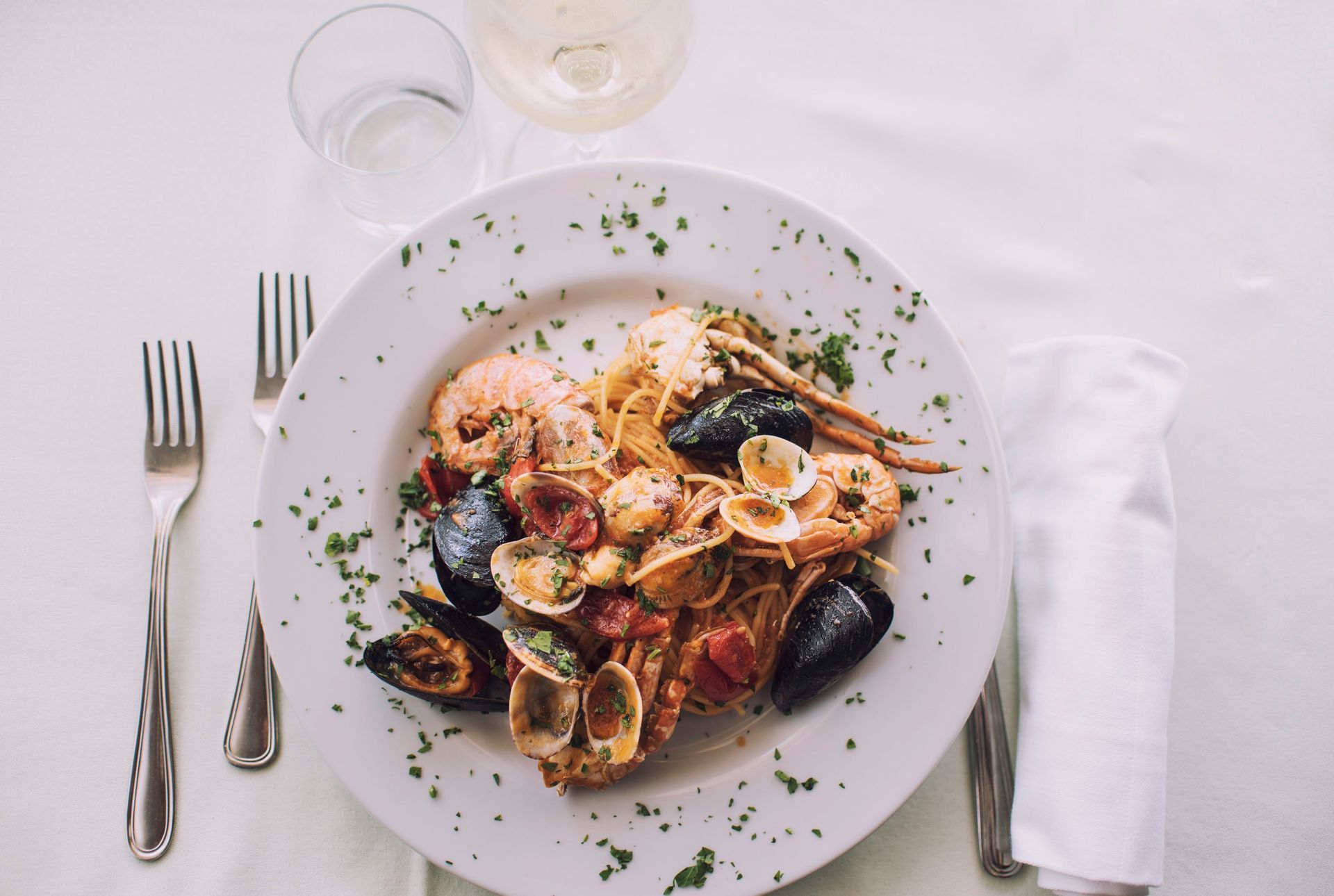 Piatto di pasta ai frutti di mare su piatto bianco, con crostacei, cozze e pomodori, apparecchiato.