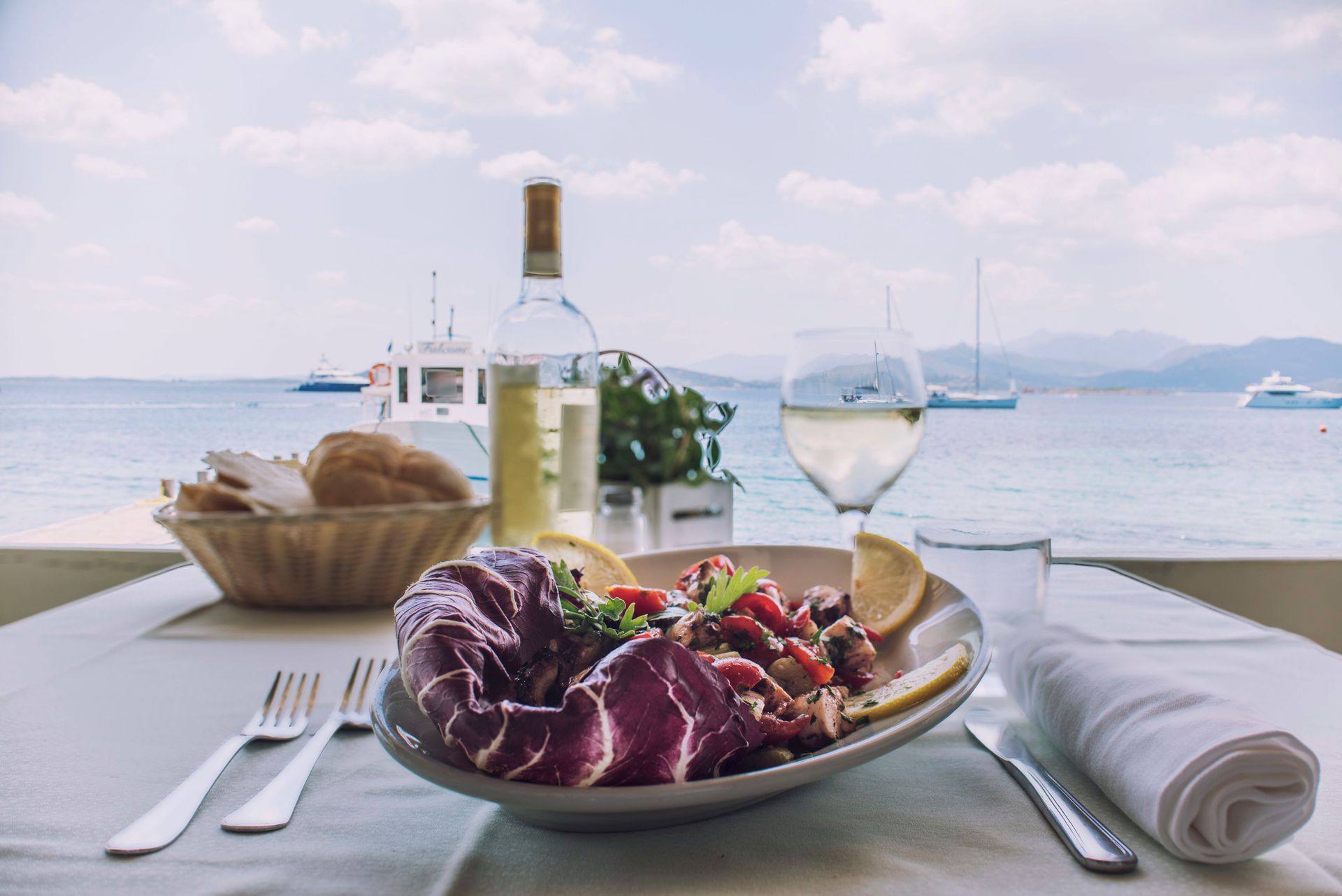 Piatto di frutti di mare, vino bianco e pane, servito su un tavolo con vista sul mare tranquillo.