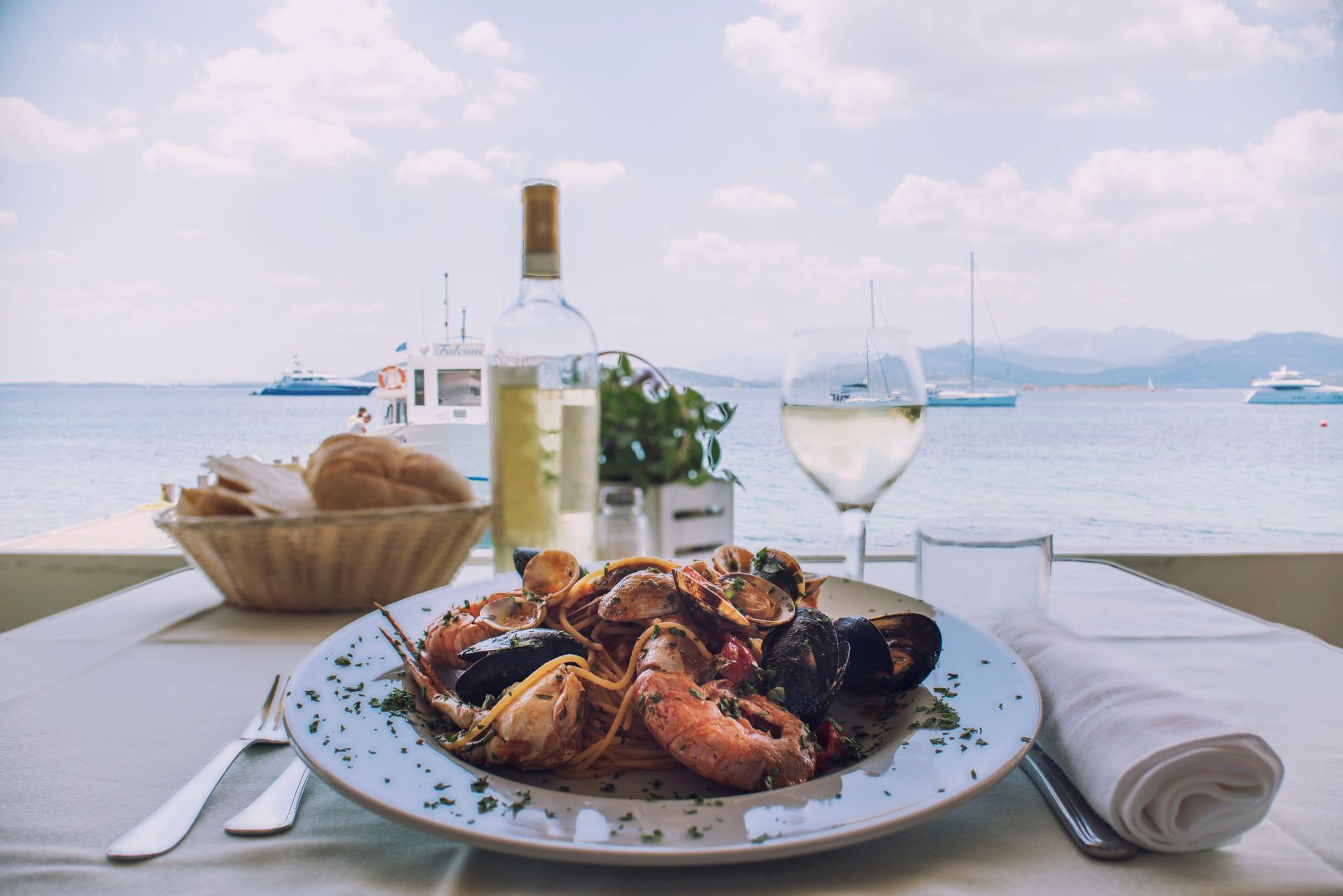Piatto di pasta ai frutti di mare con vino bianco, pane e vista sull'oceano.