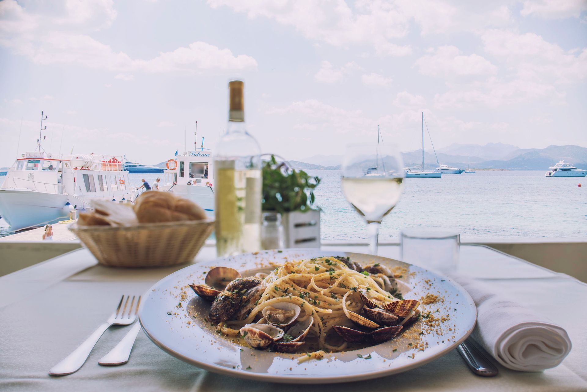 Piatto di pasta con vongole, vino bianco e pane in un ristorante sul lungomare.