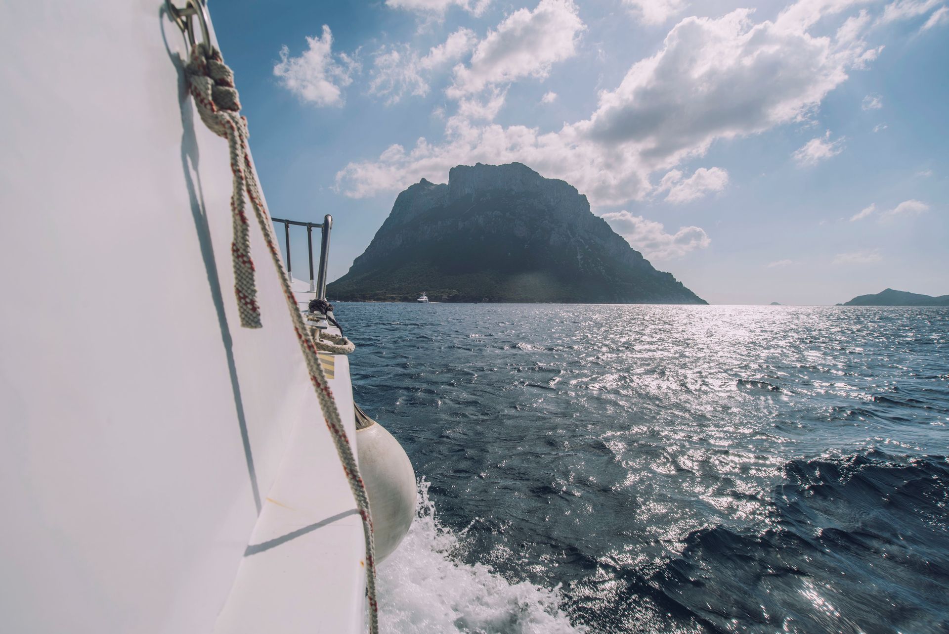 La barca naviga sul mare blu verso un'isola rocciosa sotto un cielo soleggiato.