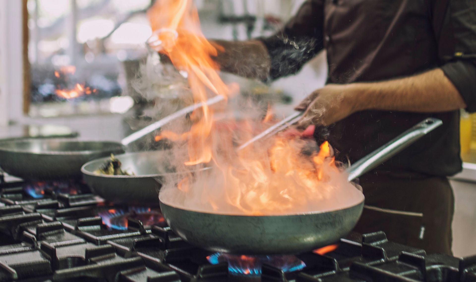 Uno chef flamba il cibo in una padella con le fiamme che salgono alte sul fornello.