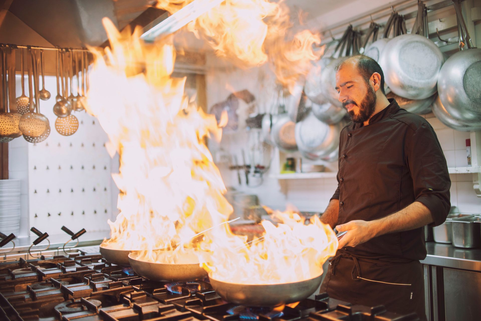 Uno chef flamba il cibo in due padelle, creando grandi fiamme in cucina.