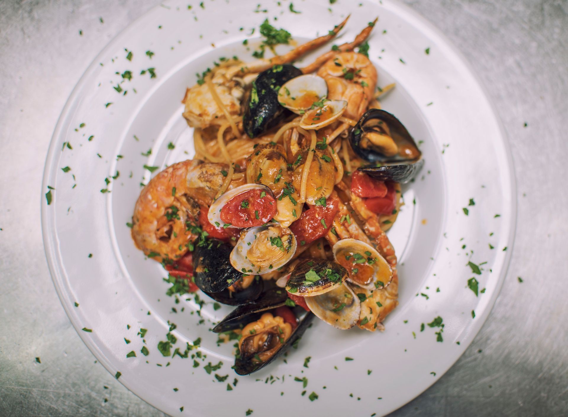 Pasta ai frutti di mare con gamberi, cozze, vongole e pomodori su un piatto bianco, cosparsa di prezzemolo.