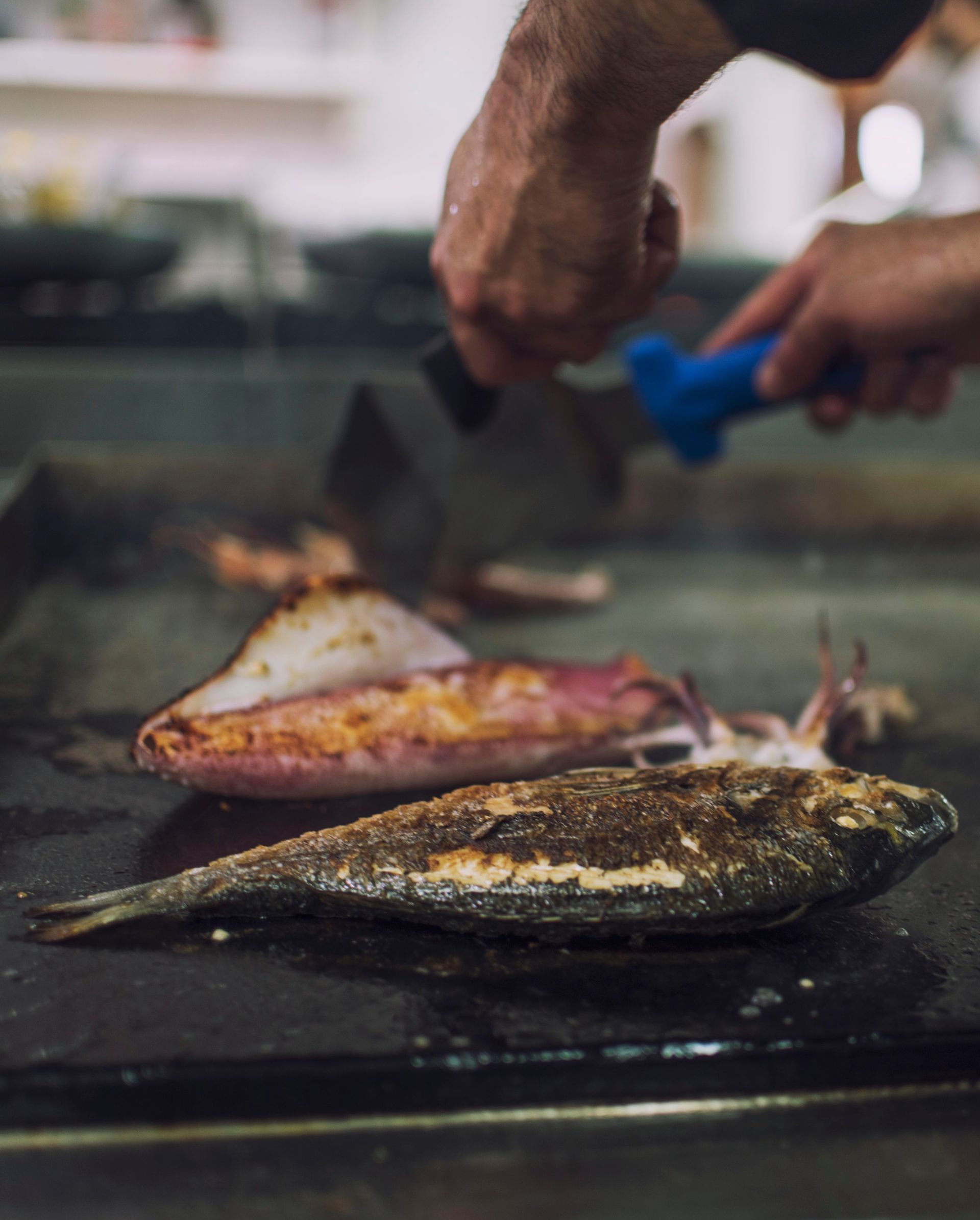Chef che griglia un pesce intero su una piastra. Con una spatola in mano.