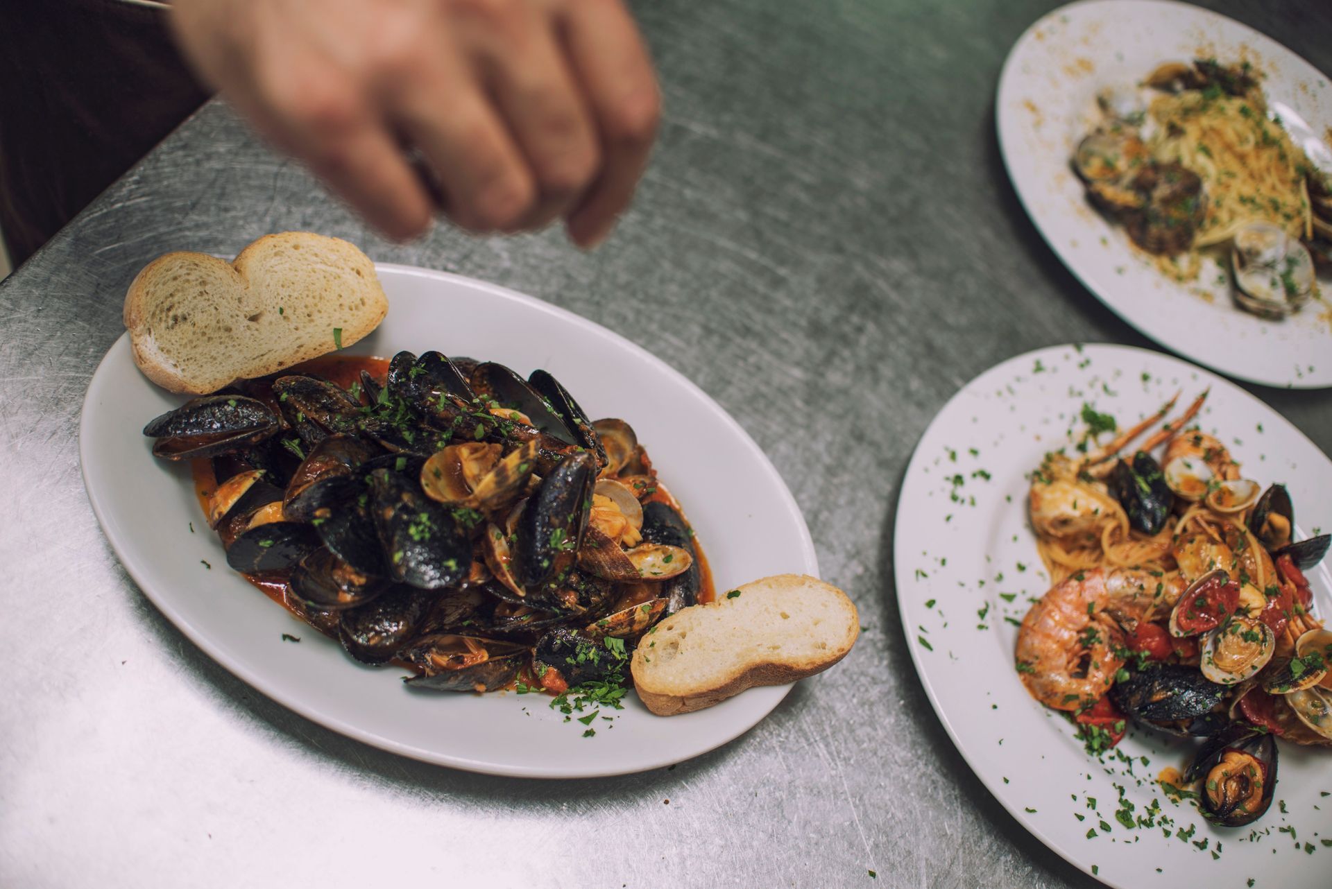 Piatti di pesce: cozze, pasta e gamberi, guarniti su una superficie in acciaio inox.