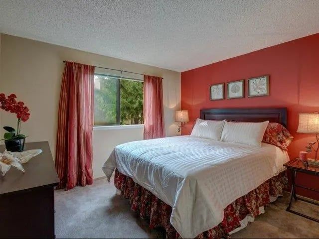 Bedroom with a king bed, white linens, red accent wall, and a window with pink curtains.