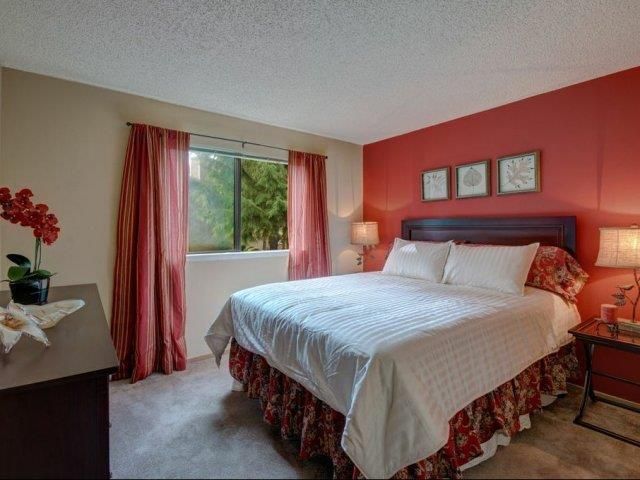 Bedroom with a king-size bed, white bedding, red accent wall, and pink-curtained window.