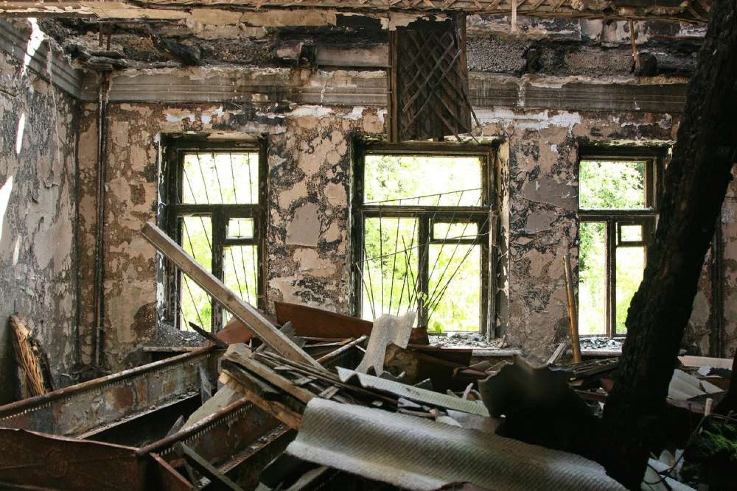 Interior view of a damaged building with debris. Windows in the background with visible forest, decaying walls.