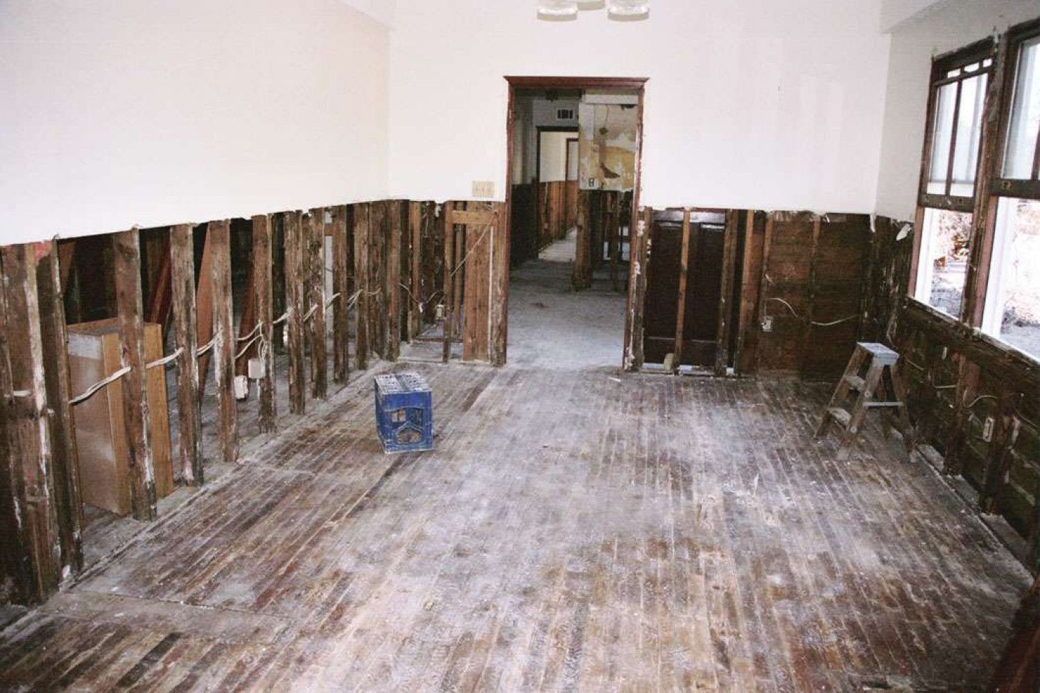 Room under renovation; walls stripped to studs, damaged flooring, a doorway and a window.