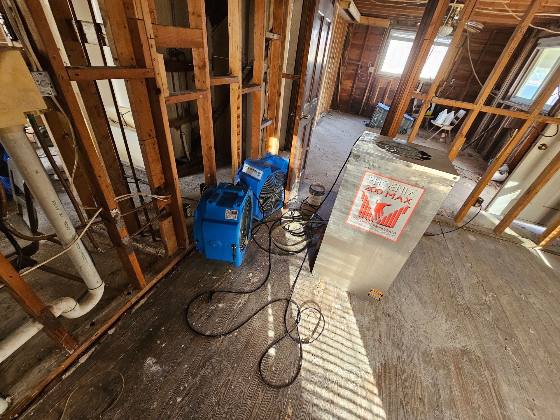 Interior construction site with blue air movers; exposed wooden framing, sunlight.