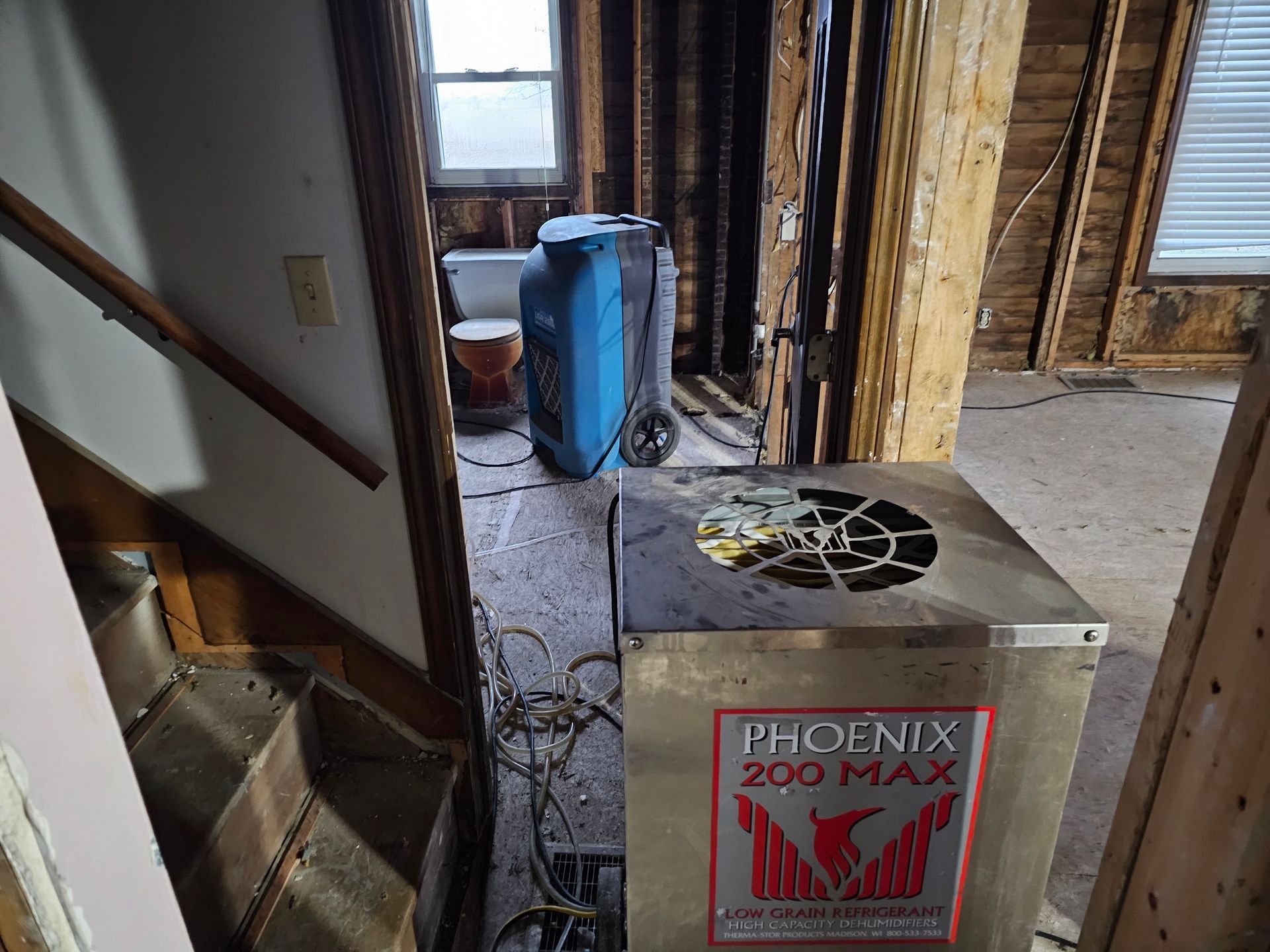 Dehumidifier in a room undergoing renovation, near a staircase. The room has exposed framing and a window.
