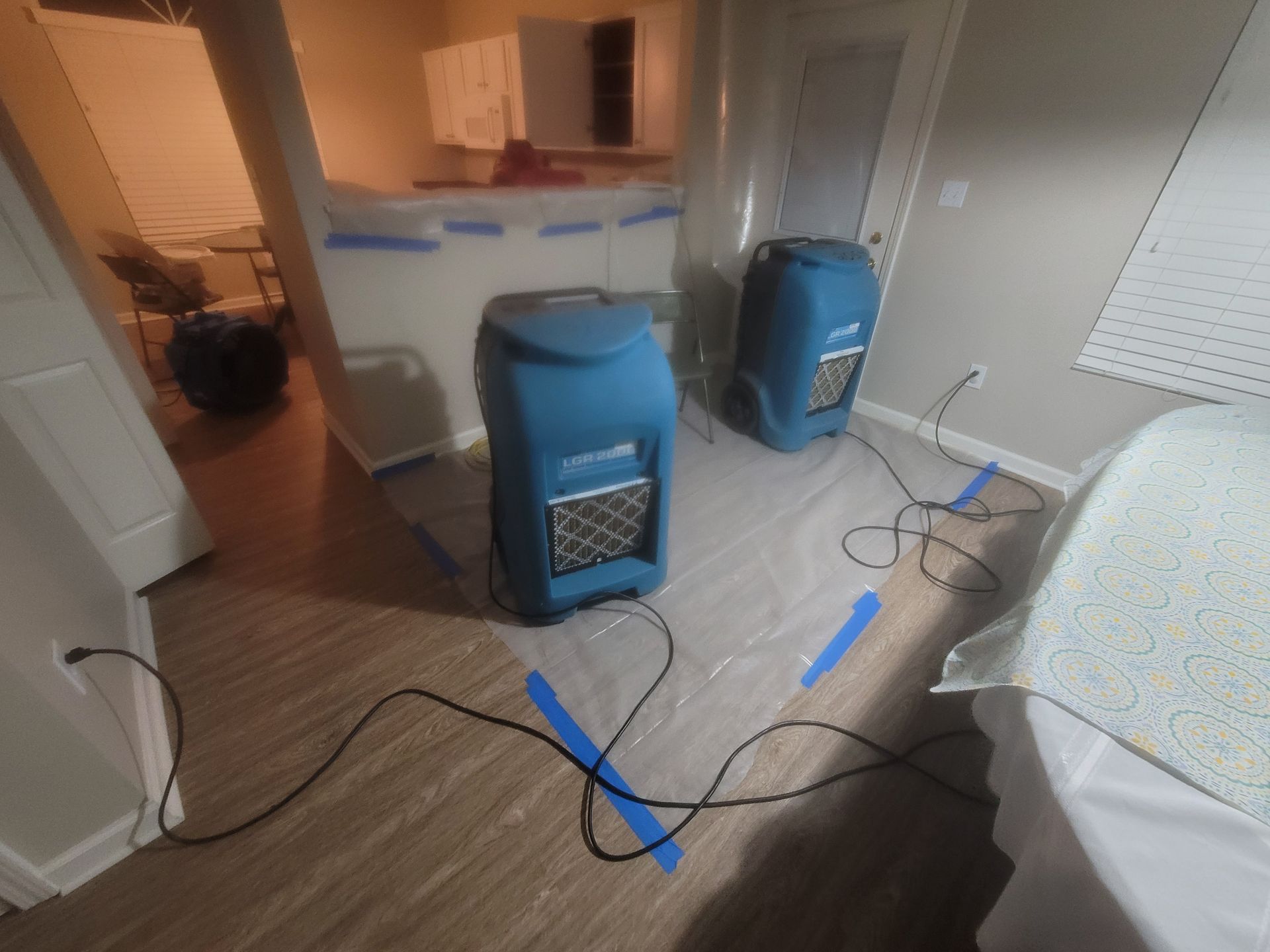 Two blue dehumidifiers on a plastic sheet in a room, drying the floor.