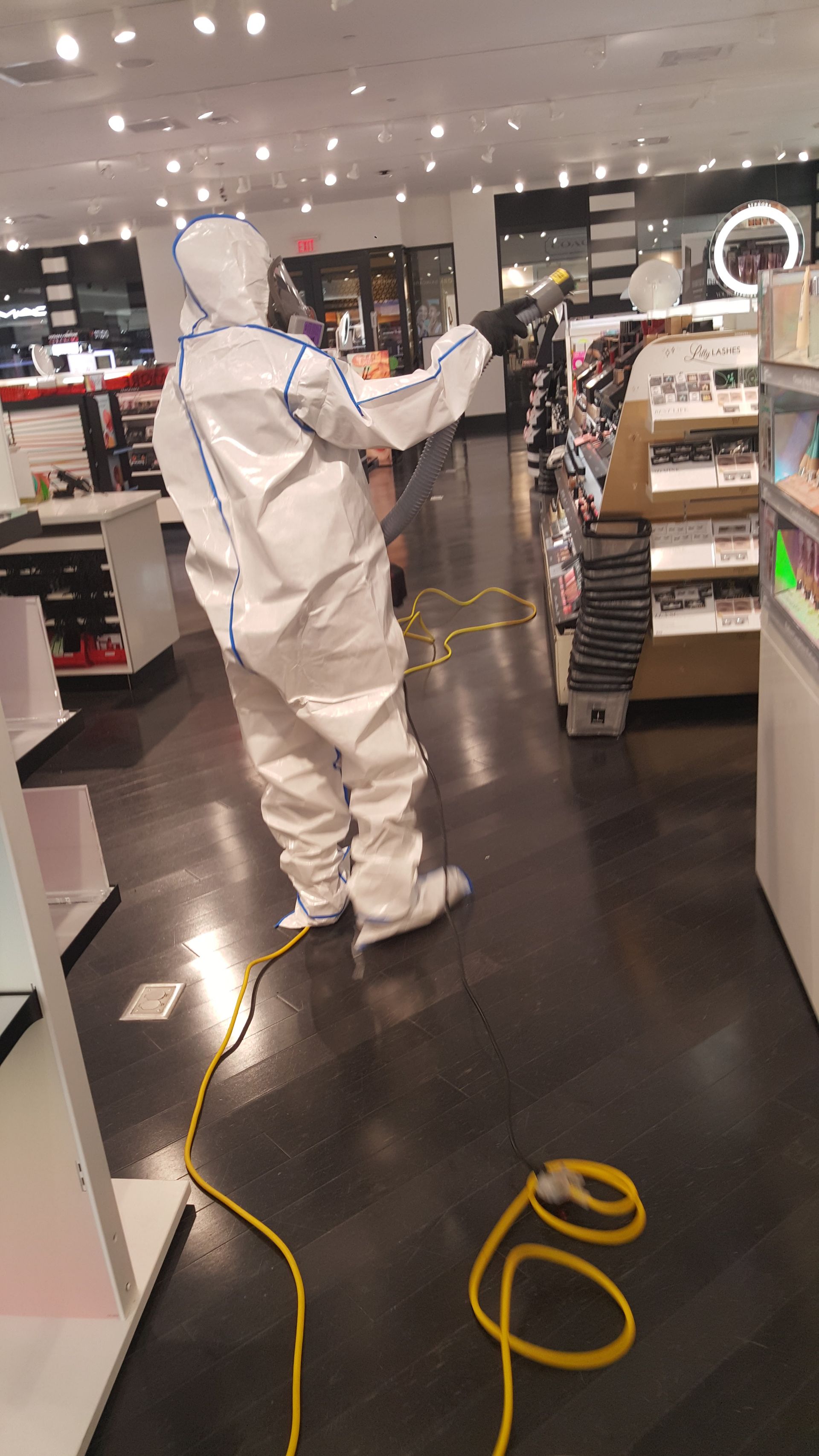 Person in protective suit disinfecting a store with a yellow hose.
