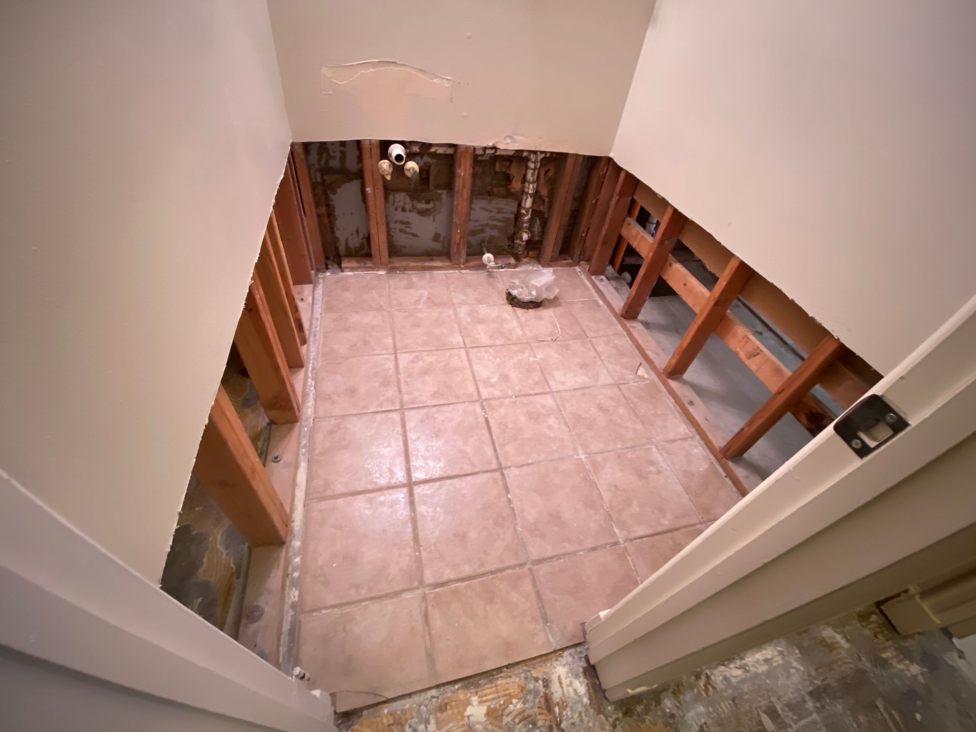 Bathroom renovation, walls open to studs, existing tile floor, beige and brown tones.