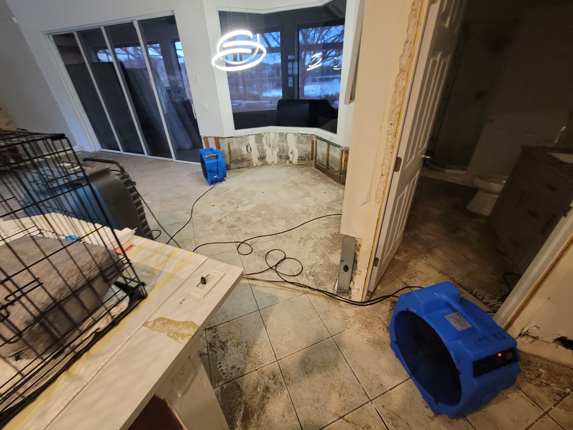 Two blue dehumidifiers in a room with water damage on the walls and floor.