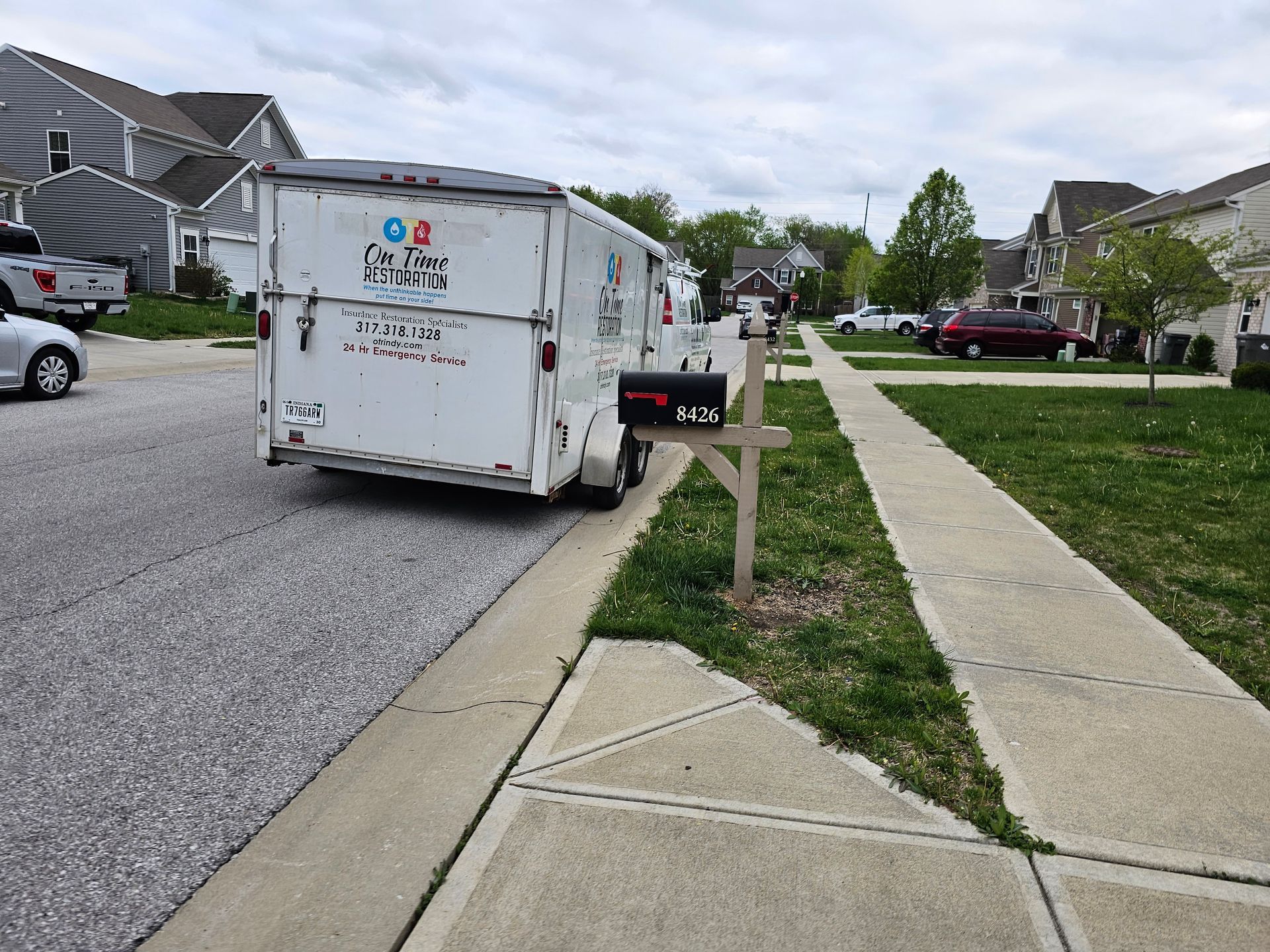 White trailer parked on a residential street next to a sidewalk and mailbox.