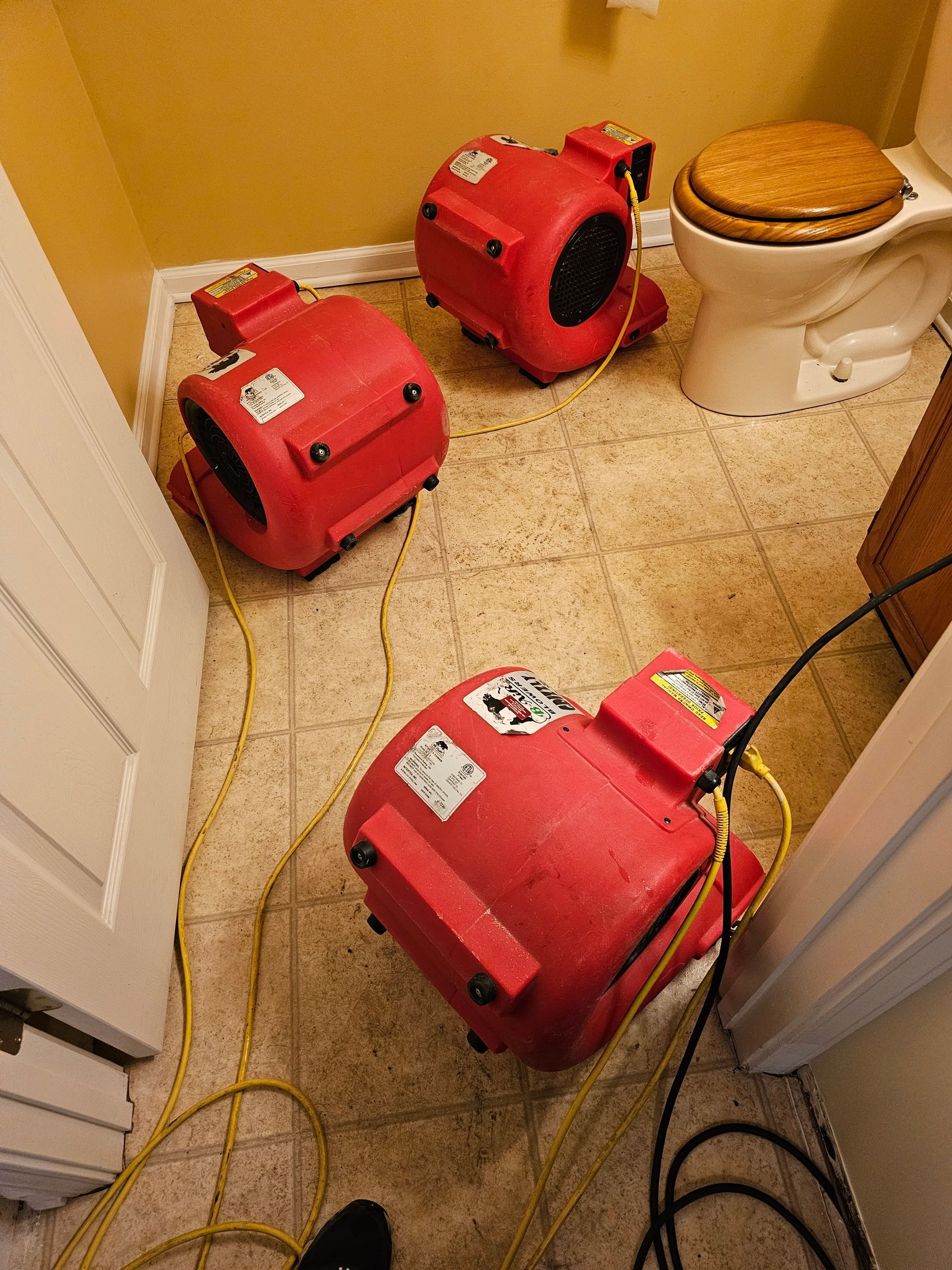 Three red air movers drying a bathroom floor near a toilet.