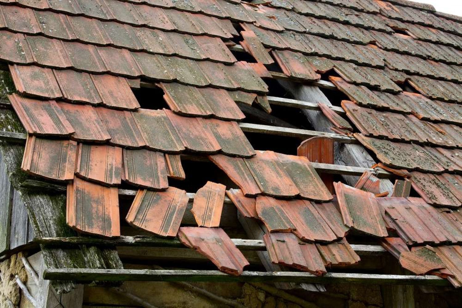 Damaged red tile roof showing exposed wooden beams and structural damage.