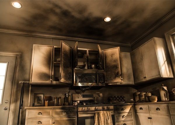 Burnt kitchen with smoke-stained cabinets, appliances, and walls, damage from a fire.